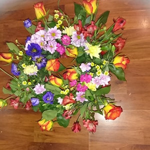 Puede incluir: Un ramo de flores colorido en tonos de rojo, naranja, amarillo, rosa, morado y blanco. El ramo incluye rosas, claveles y otras flores.