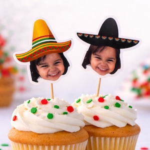 Könnte beinhalten: Zwei Cupcakes mit weißem Zuckerguss, verziert mit roten und grünen Streuseln. Jeder Cupcake ist mit einem lächelnden Gesicht mit Sombrero gekrönt. Die Cupcakes stehen auf einer weißen Oberfläche mit verstreuten Streuseln.