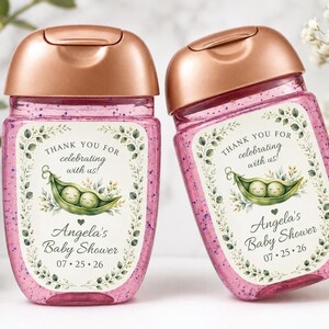 Two hand sanitizer bottles filled with pink glitter gel and topped with rose gold caps stand side by side, featuring custom pea pod labels.