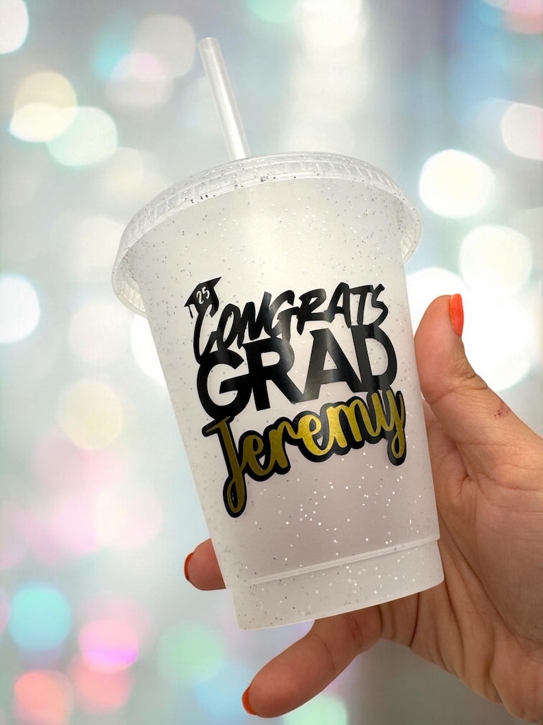May include: A white glitter tumbler with a black and gold sticker that says "Congrats Grad Jeremy".