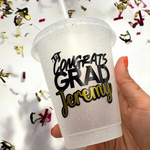May include: White glitter tumbler with a black and gold sticker that says "Congrats Grad Jeremy".