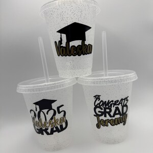 May include: Three clear plastic cups with glitter, each with a different graduation design. One cup has a black graduation cap and the name "Valeska" in gold lettering. Another cup has the year "2025" and the name "Valeska" in gold lettering. The third cup has the text "Congrats Grad Jeremy" in black lettering.
