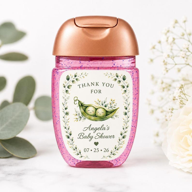 A single hand sanitizer bottle filled with pink glitter and a rose gold cap displays a custom baby shower label with a pea pod illustration.