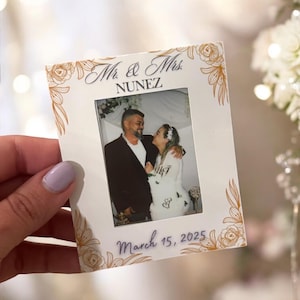 Könnte beinhalten: Weißer Fotorahmen mit goldenen floralen Akzenten. Der Rahmen enthält ein Foto eines Paares mit dem Text "Mr. & Mrs. NUNEZ" und "March 15, 2025".
