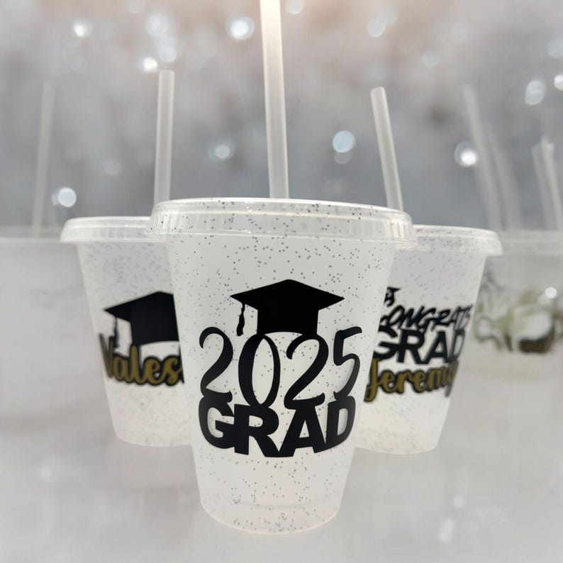May include: Set of clear plastic cups with glitter, decorated with black graduation caps and the text "2025 GRAD".