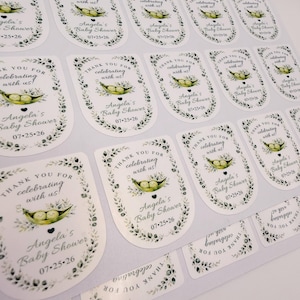 A full sheet of printed custom baby shower labels features a watercolor pea in a pod illustration and personalized text.