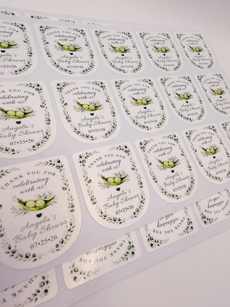 A full sheet of printed custom baby shower labels features a watercolor pea in a pod illustration and personalized text.