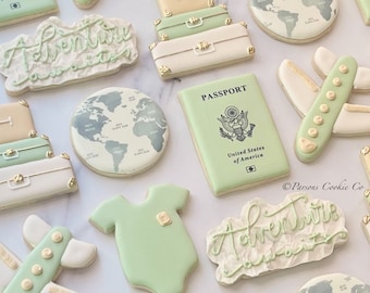 May include: A set of decorated sugar cookies with a travel theme. The cookies feature images of suitcases, airplanes, a passport, a globe, and the words "Adventure awaits".