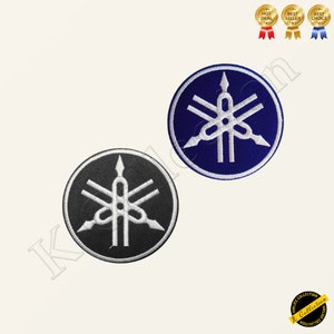 Op de afbeelding: Twee geborduurde patches met het Yamaha-logo. Eén patch is zwart met witte stiksels, de andere is blauw met witte stiksels.