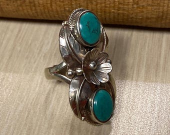 May include: A silver ring with two turquoise stones set in a floral design.