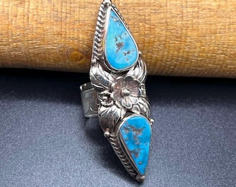 May include: A silver ring with two turquoise stones set in a floral design. The ring is shaped like a teardrop and has a textured band.