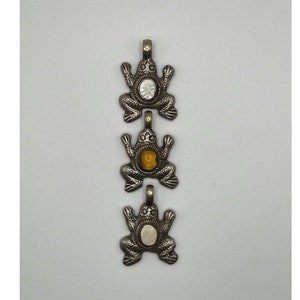 May include: Three silver frog charms with different colored stones in the center. The top and bottom charms have white stones, and the middle charm has a yellow stone.