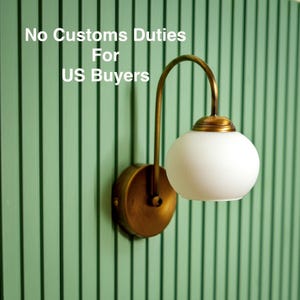 Könnte beinhalten: Wandleuchte aus Messing mit weißem Kugelschirm, montiert an einer grün gestreiften Wand. Der Text "No Customs Duties For US Buyers" ist sichtbar. Ein dekoratives Element für das Zuhause.