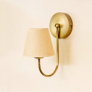 May include: A brass wall sconce with a curved arm and a beige fabric lampshade.