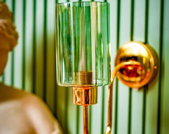 May include: A gold wall sconce with a green glass shade. The shade has vertical lines and a rounded top. The sconce has a curved arm and a round base.