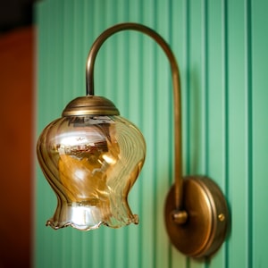 Puede incluir: Una lámpara de pared de latón con una pantalla de vidrio ámbar de tono dorado. La pantalla tiene un borde festoneado y un diseño ondulado y texturizado.