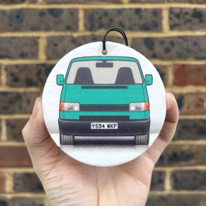 May include: A circular air freshener with a teal van design. The van has black details, headlights, and a number plate displaying "Y594 WKF". A black string is attached for hanging.