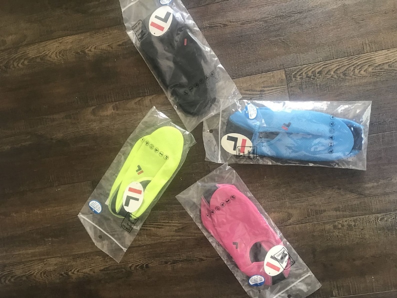 May include: Four pairs of water shoes in individual plastic packaging. The shoes are in black, blue, green, and pink. Each pair has a white "FILA" logo on the side.