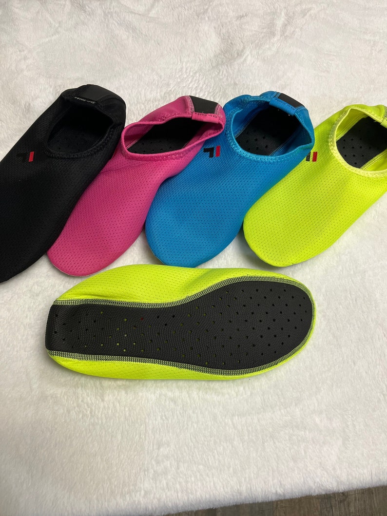 May include: Five pairs of water shoes in different colors: black, pink, blue, and two pairs of neon green. The shoes are made of a mesh material with a black rubber sole.
