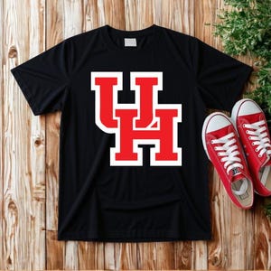 May include: A black short-sleeved t-shirt featuring a large, bold red and white block letter UH logo centred on the chest. The shirt is displayed alongside a pair of red canvas trainers with white laces and white rubber soles.