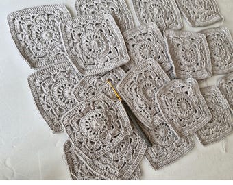 May include: A collection of crocheted squares in a light gray color, arranged in a pattern on a white surface. The squares have a delicate, intricate design with a central circle.