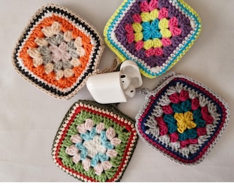 Op de afbeelding: Vier kleurrijke gehaakte vierkanten met een wit AirPod-hoesje in het midden. De vierkanten zijn gemaakt van garen in verschillende kleuren en hebben een granny square-patroon.
