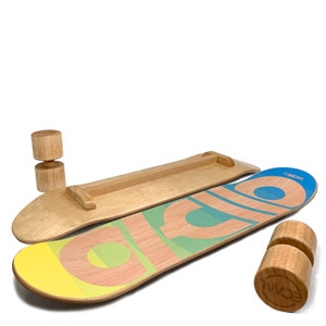 May include: Two wooden balance boards with a light wood finish. One board has a colorful design with the word "SCML" and the other is plain. Two wooden rollers are also included. The boards are designed for balance training.