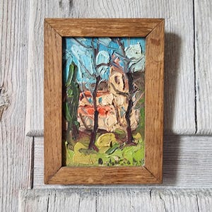 Peut inclure: Une peinture à l'huile dans un cadre en bois rectangulaire représentant un paysage avec des coups de pinceau épais. La scène montre des arbres aux troncs sombres sur un ciel bleu clair, avec un bâtiment beige et du feuillage vert.