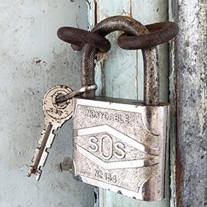 Peut inclure: Un cadenas en métal vieilli avec une clé insérée. Le cadenas porte l'inscription "INOXYDABLE" et "SOS No 134". La clé est argentée et a une tête circulaire. Une chaîne rouillée sécurise le cadenas.