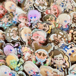 May include: A collection of colorful acrylic charms featuring various cartoon characters. The charms showcase a variety of designs, including characters with different hairstyles, outfits, and expressions. The charms are clear with a glossy finish.