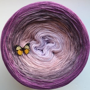 May include: A ball of yarn with a gradient of purple, pink and white colours. A small butterfly is placed on the yarn ball.
