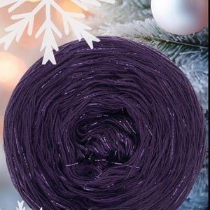 May include: A deep purple ball of yarn with silver metallic strands. The yarn is tightly wound and has a subtle sheen. The background features a white snowflake and a Christmas tree with a white bauble.