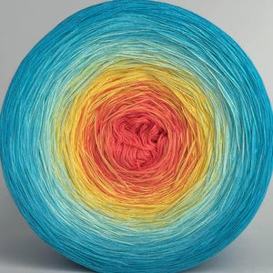 Peut inclure: Une grosse pelote de laine avec un dégradé de couleurs, passant d'un bleu turquoise vif à l'extérieur au rouge corail au centre. Des teintes jaunes et oranges créent un dégradé chaud.