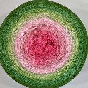 K&ouml;nnte beinhalten: Eine Garnrolle mit einem Farbverlauf von Gr&uuml;n, Rosa und Wei&szlig;. Das Garn ist zu einer Kugel gewickelt.