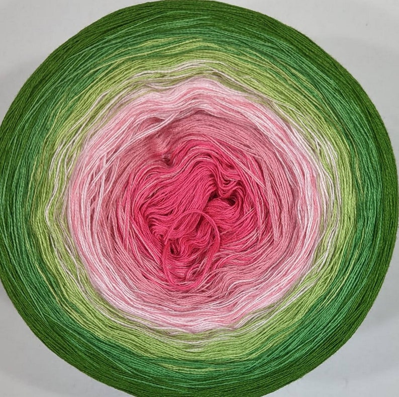 K&ouml;nnte beinhalten: Eine Garnrolle mit einem Farbverlauf von Gr&uuml;n, Rosa und Wei&szlig;. Das Garn ist zu einer Kugel gewickelt.