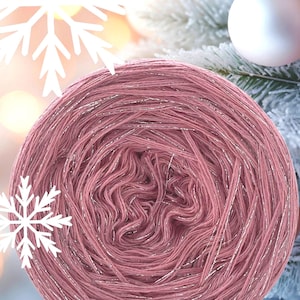 May include: A large ball of pink yarn with silver metallic threads. The yarn is in a circular shape, with the strands visible. The background includes Christmas decorations and a snowflake.