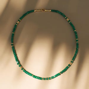 May include: A delicate green gemstone necklace with gold accents. The necklace is made of small, faceted beads and is strung on a thin gold chain.