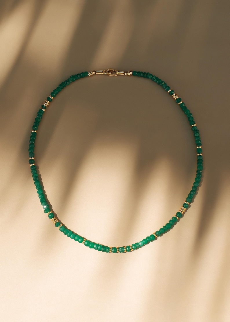 May include: A delicate green gemstone necklace with gold accents. The necklace is made of small, faceted beads and is strung on a thin gold chain.