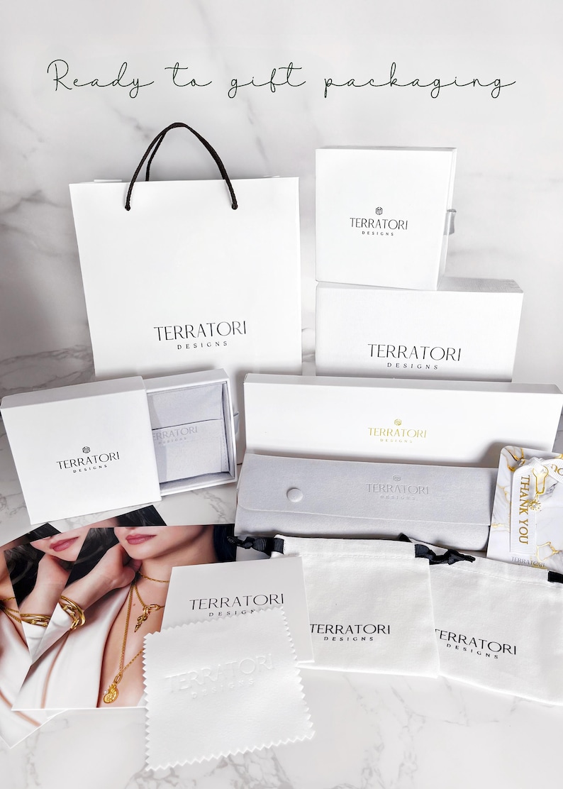 May include: A collection of white gift boxes and bags with the logo "Terratori Designs" printed on them. The boxes and bags are arranged on a white marble surface. There are also several white cloth bags with the same logo. One of the bags has a "Thank You" tag attached to it.