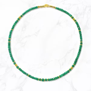 May include: A green gemstone beaded necklace with gold accents. The necklace is made of small, faceted beads and has a simple, elegant design.