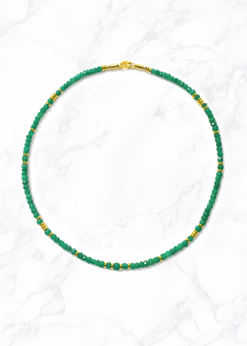 May include: A green gemstone beaded necklace with gold accents. The necklace is made of small, faceted beads and has a simple, elegant design.