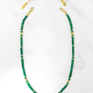 May include: A delicate green and gold beaded necklace. The necklace is made of small, round green beads with gold accents. The necklace is approximately 46 cm long and has a lobster clasp closure.