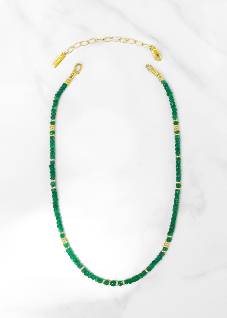 May include: A delicate green and gold beaded necklace. The necklace is made of small, round green beads with gold accents. The necklace is approximately 46 cm long and has a lobster clasp closure.