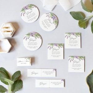 Può includere: Set di partecipazioni di nozze con fedi d'oro in una scatola esagonale bianca, biglietti rotondi e quadrati e biglietti rettangolari. I biglietti presentano un motivo floreale con accenti lavanda e verdi e la parola "Grazie".