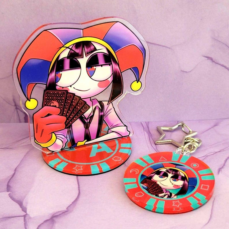 May include: A clear acrylic stand-up figure and a keychain featuring a cartoon character in a jester hat holding playing cards. The stand has a red base with the letter "A". The keychain is a red circle with a star-shaped clasp.
