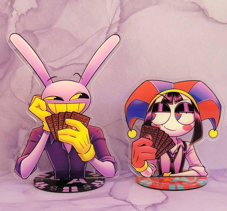 May include: Two acrylic standees featuring cartoon characters. One is a pink rabbit with yellow gloves and a purple suit, holding cards. The other is a jester-like character with a red, blue, and yellow hat, also holding cards. Both standees have detailed bases.