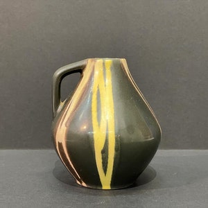 May include: A small, dark green ceramic vase with a handle. The vase has a unique design with yellow and pink stripes.