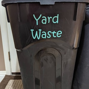 May include: Black plastic yard waste bin with a turquoise sticker that says "Yard Waste".