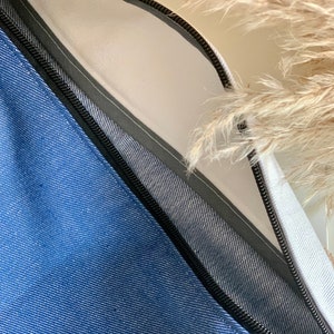 Puede incluir: Una bolsa de cremallera de mezclilla azul con una etiqueta blanca que dice "Louma".