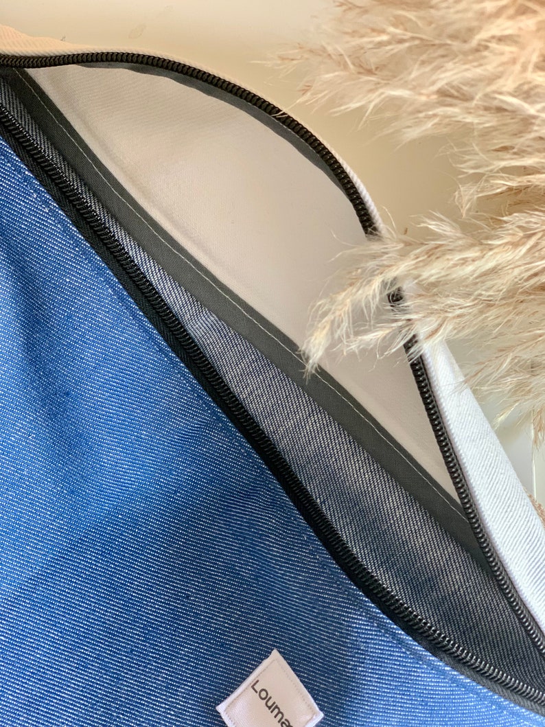 Puede incluir: Una bolsa de cremallera de mezclilla azul con una etiqueta blanca que dice "Louma".